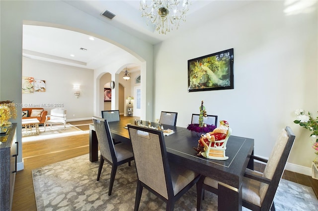 dining area featuring arched walkways, visible vents, baseboards, a chandelier, and wood finished floors