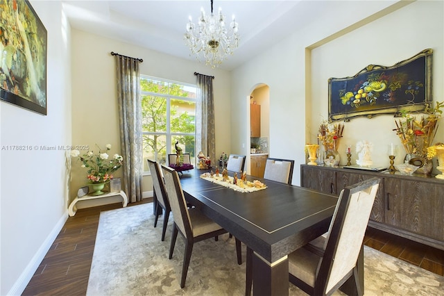 dining area featuring arched walkways, a chandelier, wood finished floors, and baseboards
