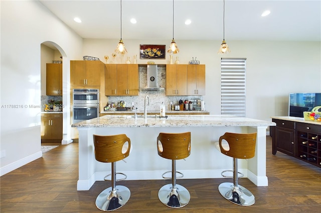 kitchen with double oven, a sink, dark wood-type flooring, and wall chimney range hood