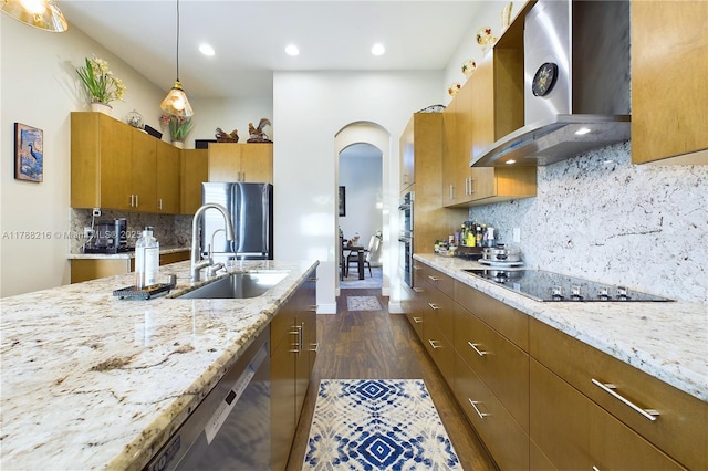 kitchen with wall chimney range hood, a sink, arched walkways, dark wood finished floors, and appliances with stainless steel finishes
