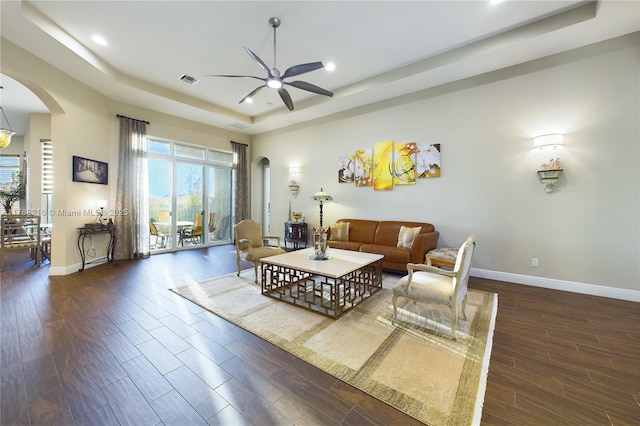 living area with baseboards, arched walkways, a ceiling fan, and a raised ceiling