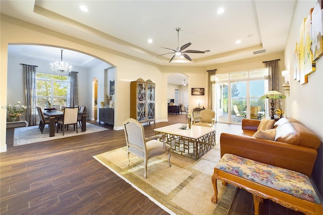 living room featuring recessed lighting, a raised ceiling, arched walkways, dark wood-style flooring, and ceiling fan with notable chandelier