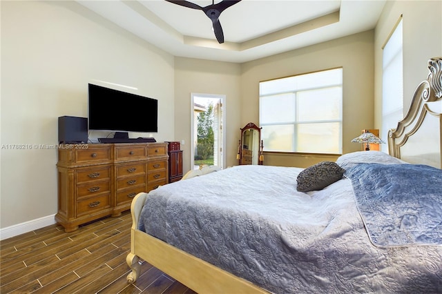 bedroom with a ceiling fan, baseboards, a raised ceiling, and dark wood finished floors