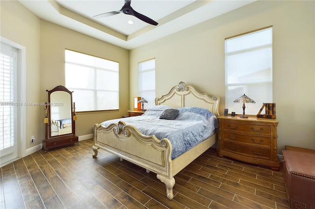 bedroom with baseboards, a ceiling fan, dark wood-style floors, and a raised ceiling