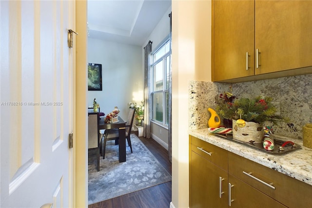 kitchen with brown cabinets, tasteful backsplash, light stone counters, and dark wood-style flooring
