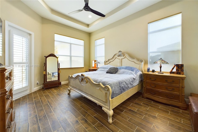 bedroom featuring a ceiling fan, baseboards, dark wood-style flooring, and a tray ceiling