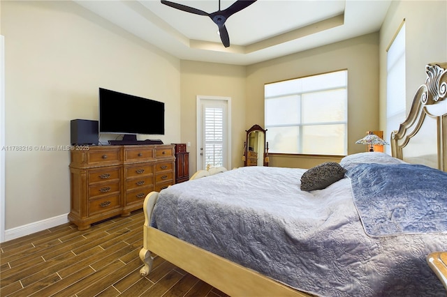 bedroom with ceiling fan, baseboards, dark wood-style floors, and a raised ceiling