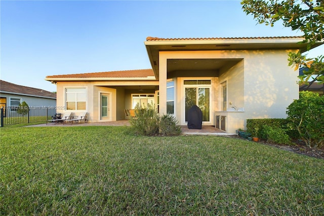 back of property featuring a tiled roof, fence, a yard, a patio, and stucco siding