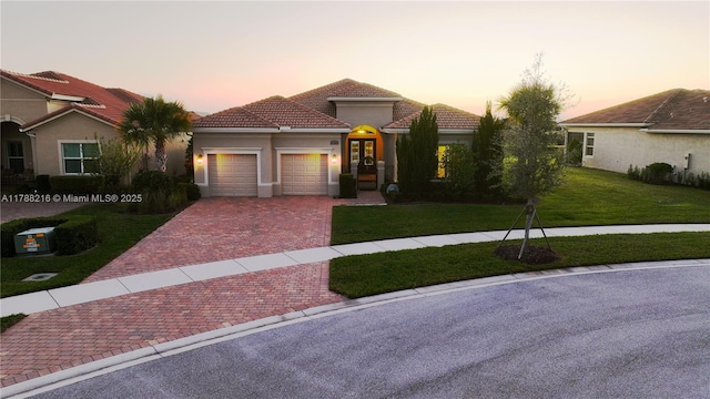 view of front of property with a yard, stucco siding, an attached garage, a tile roof, and decorative driveway
