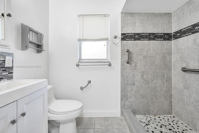 bathroom with tiled shower, tile patterned floors, toilet, vanity, and baseboards