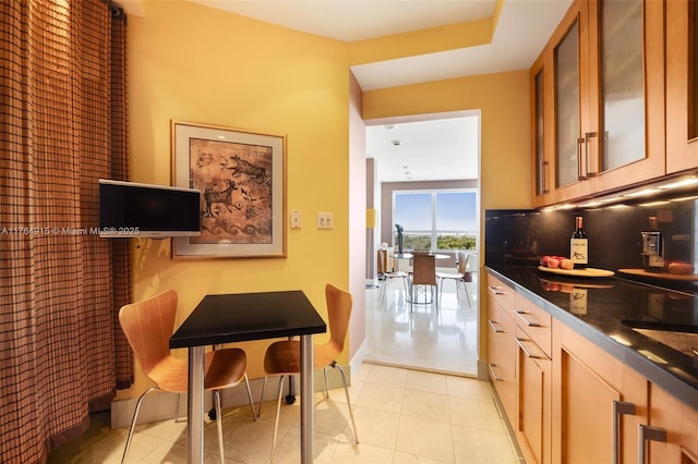 4925 Collins Ave Unit 8G, Miami Beach, FL 33140 - kitchen with brown cabinets, dark countertops, baseboards, decorative backsplash, and glass insert cabinets