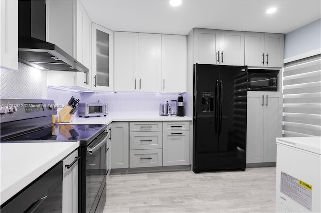 kitchen featuring light countertops, backsplash, wall chimney exhaust hood, and black appliances