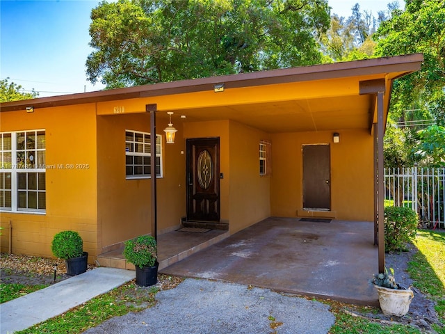 property entrance featuring concrete block siding, an attached carport, and fence