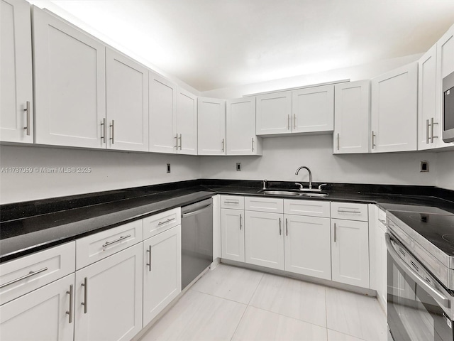 kitchen featuring stainless steel appliances, dark countertops, light tile patterned floors, a sink, and white cabinetry