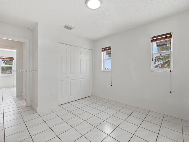 unfurnished bedroom featuring light tile patterned floors, a textured ceiling, visible vents, and a closet