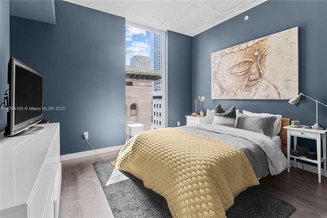bedroom featuring wood finished floors, expansive windows, and baseboards
