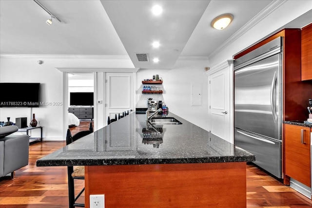kitchen featuring a breakfast bar, visible vents, a sink, built in refrigerator, and hardwood / wood-style flooring