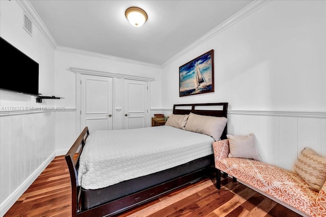 bedroom with wainscoting, ornamental molding, wood finished floors, and visible vents