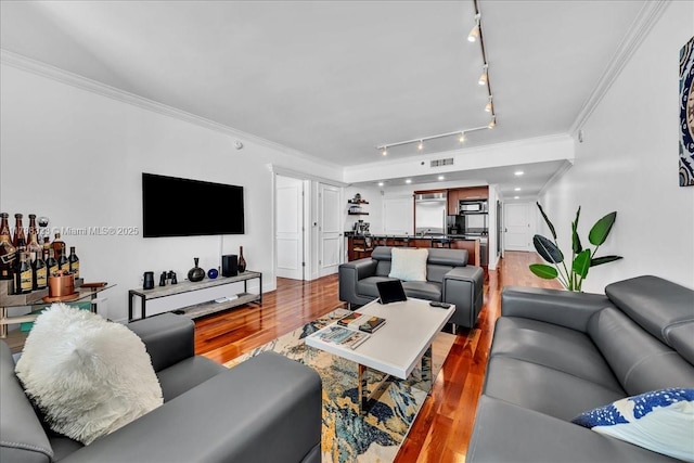 living room with track lighting, crown molding, wood finished floors, and visible vents