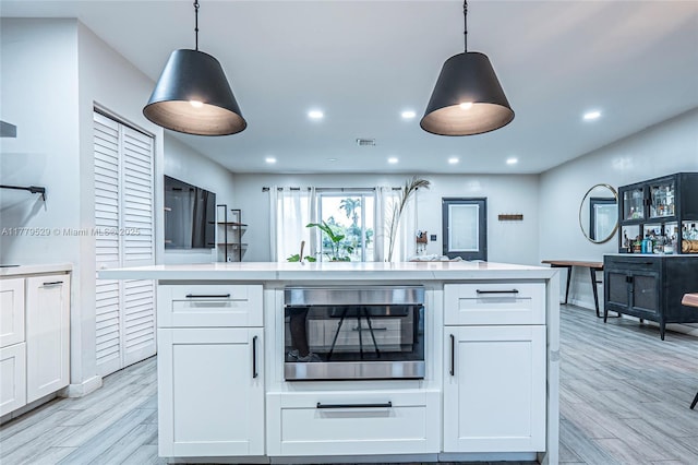 kitchen with stainless steel microwave, white cabinets, light countertops, light wood-type flooring, and decorative light fixtures