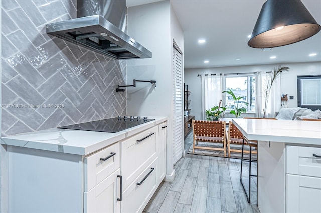 kitchen with tasteful backsplash, black electric cooktop, white cabinets, wall chimney exhaust hood, and open floor plan