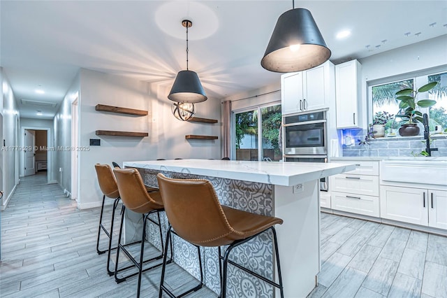 kitchen featuring a sink, stainless steel double oven, a breakfast bar area, light wood-style flooring, and white cabinets