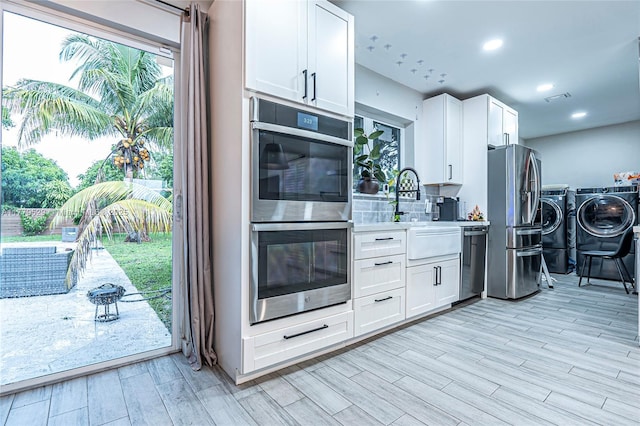 kitchen featuring light wood-style flooring, appliances with stainless steel finishes, light countertops, white cabinetry, and washer and clothes dryer