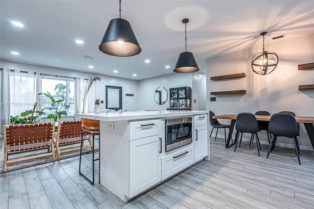 kitchen featuring stainless steel microwave, decorative light fixtures, light countertops, white cabinetry, and visible vents