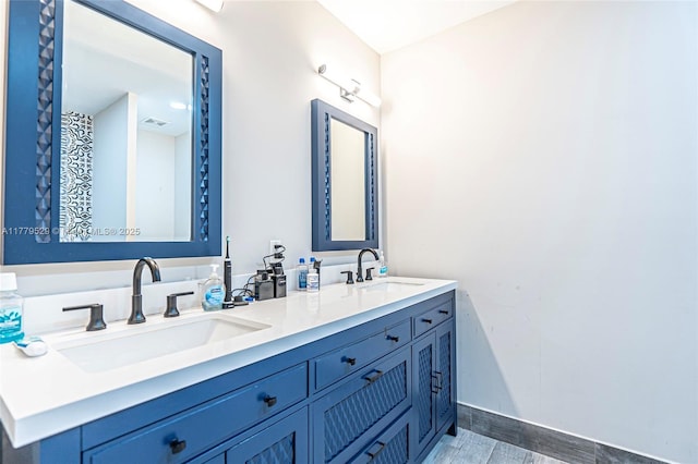 full bath with double vanity, a sink, wood finished floors, and baseboards
