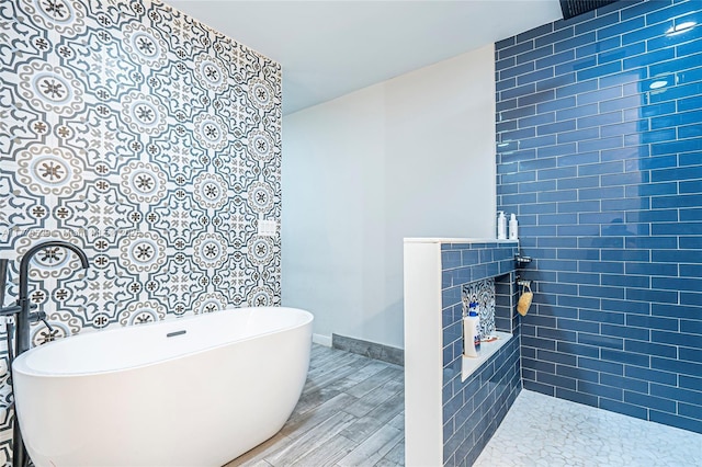 bathroom featuring a tile fireplace, tiled shower, wood finished floors, baseboards, and a soaking tub