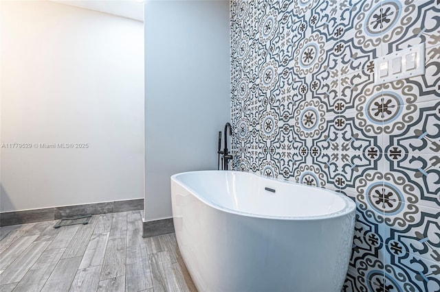 bathroom with a freestanding tub, wood finished floors, and baseboards