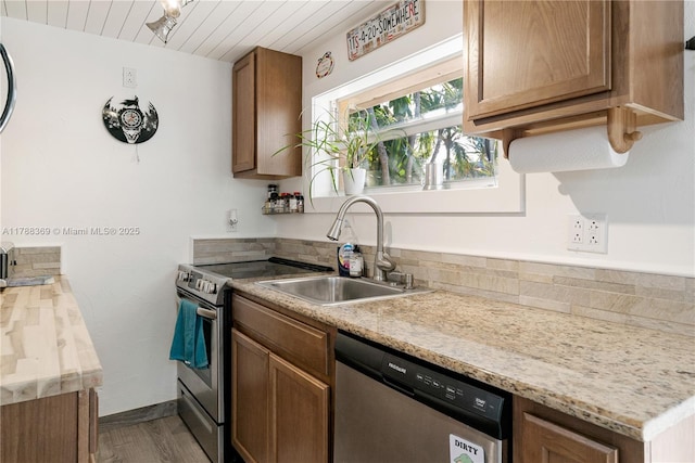kitchen featuring a sink, baseboards, brown cabinetry, appliances with stainless steel finishes, and dark wood-style flooring