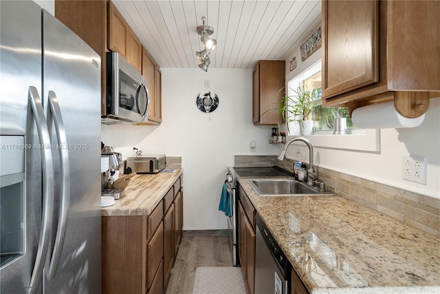 kitchen with brown cabinets, appliances with stainless steel finishes, a sink, and light wood-style flooring
