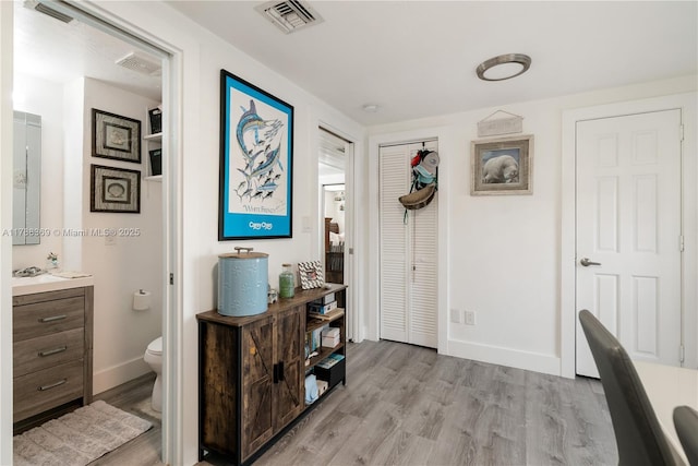 hall featuring baseboards, visible vents, and light wood-style flooring