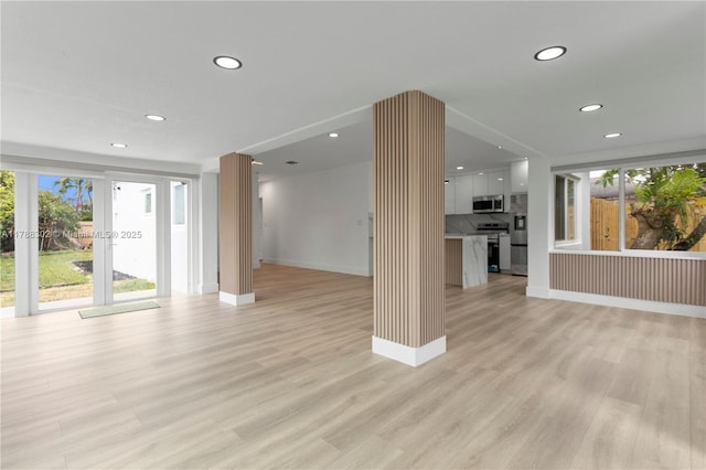 unfurnished living room with recessed lighting, light wood-type flooring, a healthy amount of sunlight, and baseboards
