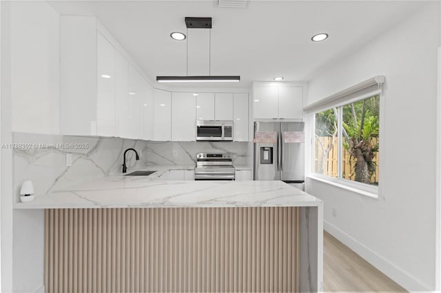 kitchen with a peninsula, a sink, modern cabinets, light stone counters, and appliances with stainless steel finishes