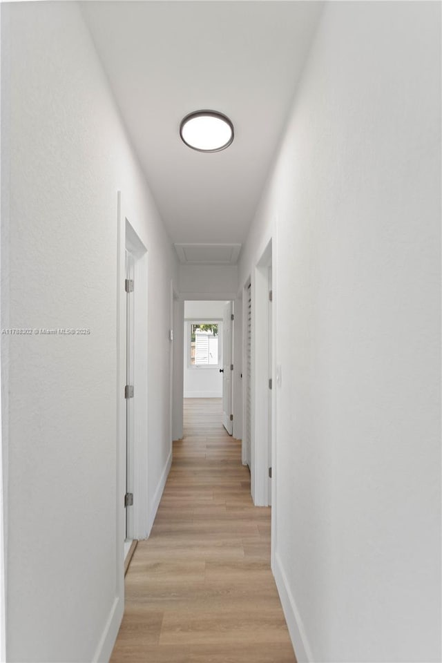 hallway featuring attic access, light wood finished floors, and baseboards