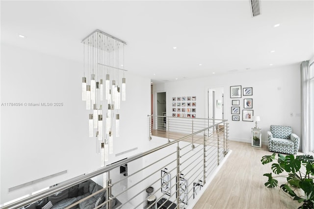 hallway with an upstairs landing, light wood-style flooring, baseboards, visible vents, and recessed lighting