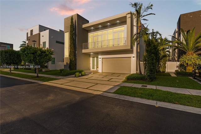 modern home with stucco siding, an attached garage, concrete driveway, and a balcony