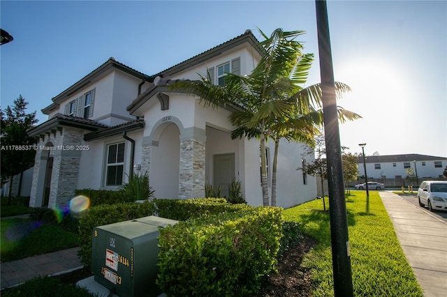 mediterranean / spanish-style house featuring stucco siding, a tile roof, stone siding, and a front yard
