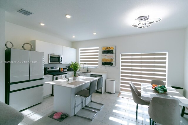 kitchen with a center island, a sink, white cabinets, appliances with stainless steel finishes, and visible vents