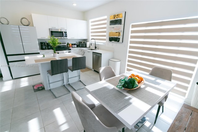 kitchen with stainless steel appliances, a center island, a sink, white cabinetry, and light countertops