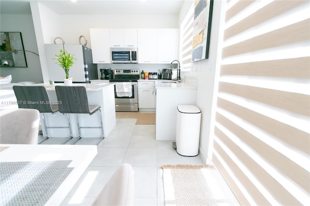 kitchen with white cabinets, stainless steel appliances, light countertops, a breakfast bar, and a sink