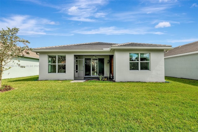 rear view of property with stucco siding, a lawn, and a ceiling fan