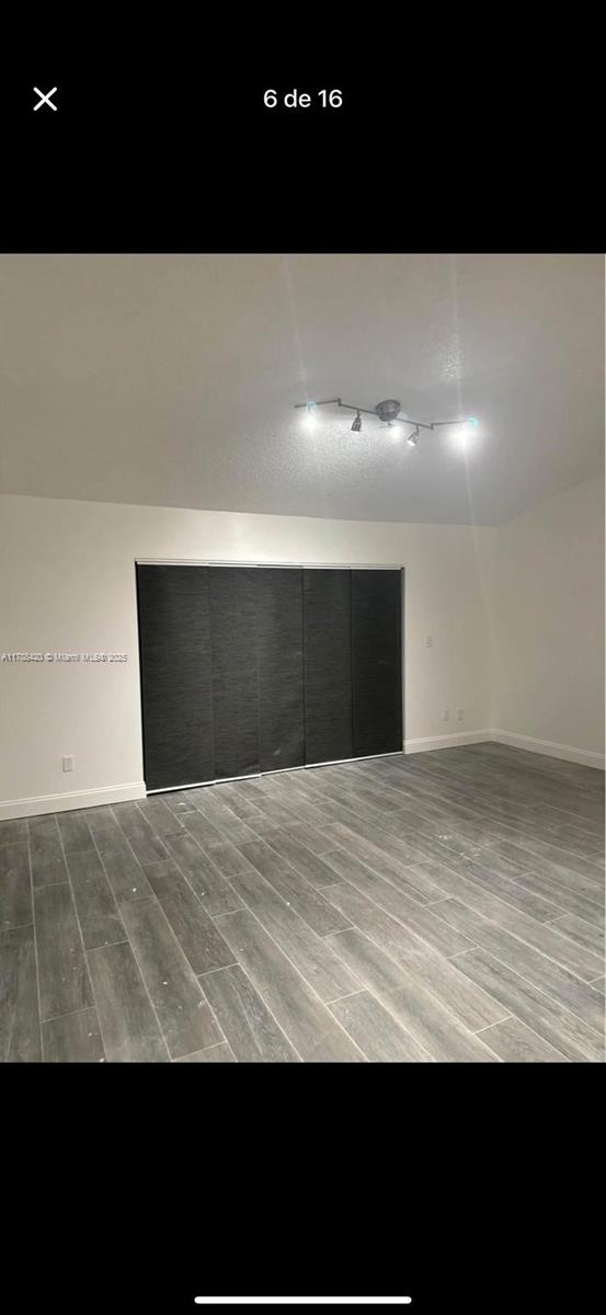 unfurnished room with track lighting, wood finished floors, and baseboards