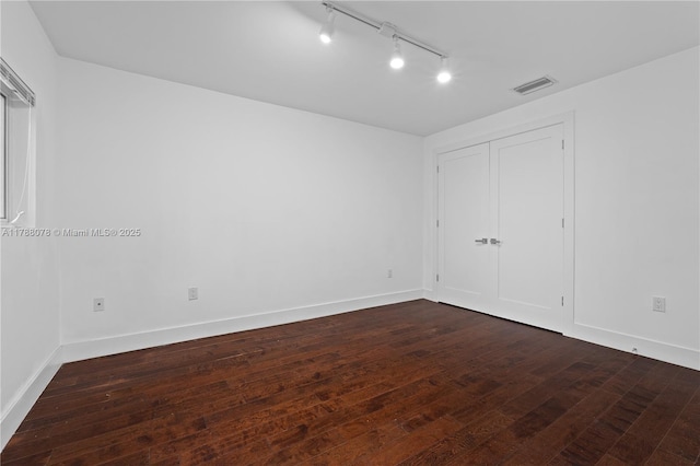 unfurnished bedroom with dark wood finished floors, rail lighting, baseboards, and visible vents