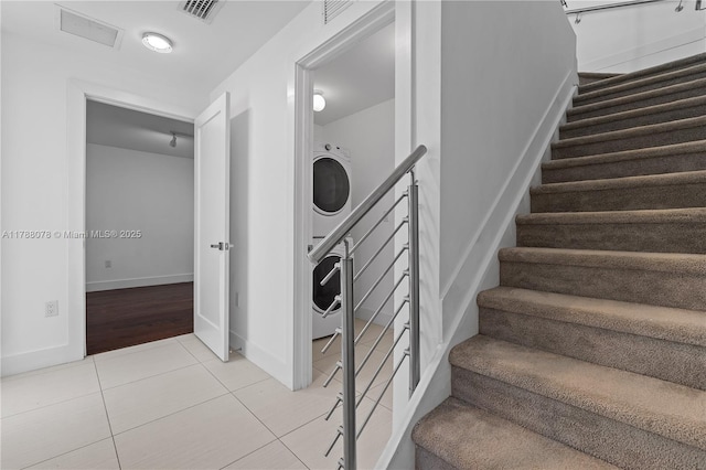 stairs with baseboards, stacked washer / dryer, tile patterned floors, and visible vents