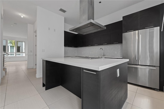 kitchen featuring island range hood, dark cabinetry, backsplash, visible vents, and freestanding refrigerator