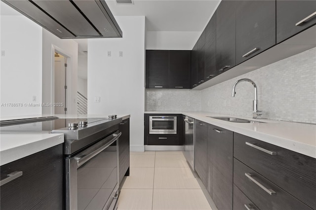 kitchen featuring light countertops, dark cabinetry, a sink, decorative backsplash, and appliances with stainless steel finishes