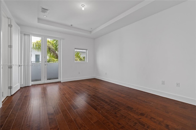 empty room with dark wood finished floors, a raised ceiling, visible vents, and baseboards